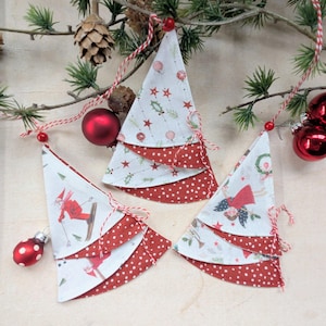 Könnte beinhalten: Drei handgefertigte Weihnachtsbaum-Ornamente. Jeder Baum besteht aus Stoffschichten, mit einer weißen oberen Schicht mit festlichen Mustern und einer roten gepunkteten Basis. Die Bäume sind an rot-weißem Garn aufgehängt.