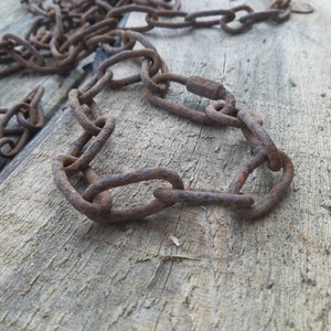 Puede incluir: Una cadena de metal oxidada con algunos eslabones formando un círculo, que yace sobre una superficie de madera desgastada.