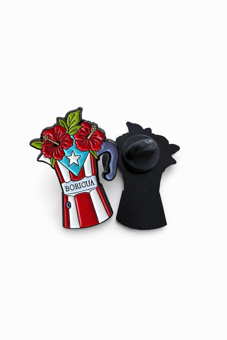 Pode incluir: Um alfinete de esmalte colorido em forma de cafeteira, com a bandeira de Porto Rico e flores de hibisco vermelhas. O alfinete tem um verso preto e a palavra "BORICUA" est&aacute; impressa na frente.