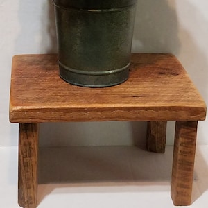 May include: A rustic wooden stool with a weathered finish, featuring a metal bucket filled with white and green hydrangea flowers.