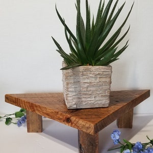 May include: A triangular wooden plant stand with three legs, made from reclaimed wood, with a succulent plant in a white brick-patterned pot on top.
