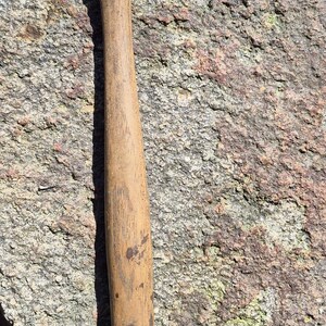 May include: A well-worn claw hammer with a wooden handle and a metal head. The hammer is resting on a rough, textured rock surface. The handle shows signs of use.