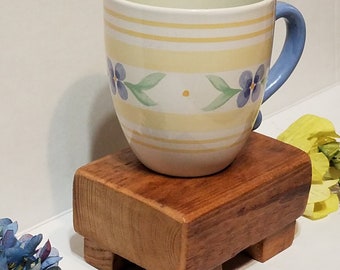 May include: A yellow and white striped mug with blue flowers and a blue handle sits on a wooden coaster with four legs.