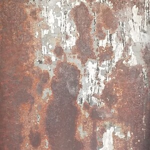May include: A close-up of a rusty metal surface with peeling paint. The surface is a mix of brown, gray, and white. The paint is peeling in large patches, revealing the rusty metal underneath.