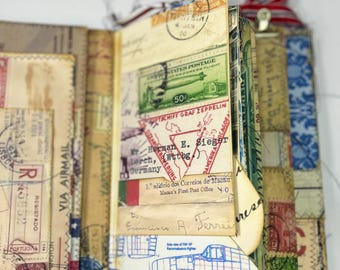 May include: A handmade journal with vintage postage stamps, airmail labels, and handwritten notes. The pages are a mix of cream and tan, with red, green, and blue accents. The journal features a variety of stamps, including a 50-cent stamp.