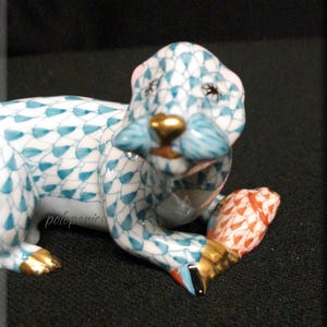 May include: A blue and white porcelain figurine of an otter holding a fish. The otter has a gold nose and whiskers. The fish is orange and white.