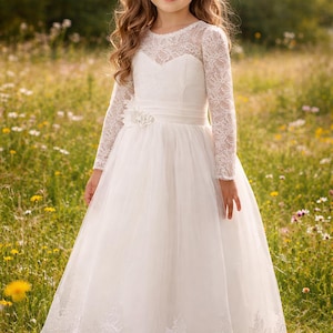 Könnte beinhalten: Ein junges Mädchen in einem weißen Spitzenkleid mit langen Ärmeln und einem weiten Rock steht in einem Feld mit Wildblumen. Das Kleid hat ein Spitzenoberteil und eine florale Verzierung an der Taille.