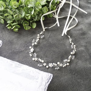 Könnte beinhalten: Ein zartes weißes Perlen- und Kristall-Brautdiadem mit floralem Design. Das Diadem liegt auf einem grauen Hintergrund mit einem weißen Spitzenstoff.