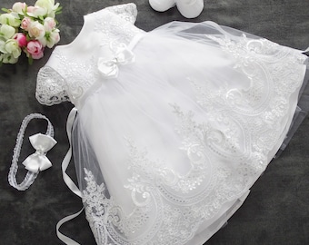 May include: White baby dress with lace detailing and a tulle skirt. The dress comes with a matching headband and shoes.