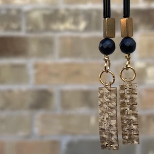 May include: A pair of gold earrings with black beads and textured rectangular charms.