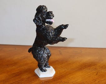 Può includere: Una statuetta in porcellana nera di un barboncino in piedi sulle zampe posteriori con le zampe anteriori alzate. Il barboncino ha la lingua rosa che sporge ed è in piedi su una base bianca.