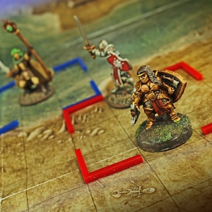 May include: Three painted miniature fantasy figures standing on a grid map. One figure in the foreground wears gold armor and carries a shield. Behind it, a figure in silver armor holds a sword and shield, and another holds a staff.