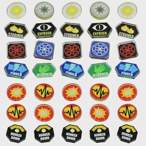 May include: A collection of game tokens with various designs and text. The tokens feature symbols like stars, explosions, and a heartbeat, along with text such as "STRAINED", "EXPOSED", "PINNED", "DISARMED", and "HUNKER DOWN".