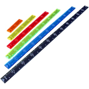 May include: Set of seven colorful rulers, each with a different color and number markings. The rulers are arranged in a triangular shape, with the longest ruler at the bottom and the shortest ruler at the top. The colors of the rulers are black, blue, green, red, yellow, orange, and purple.