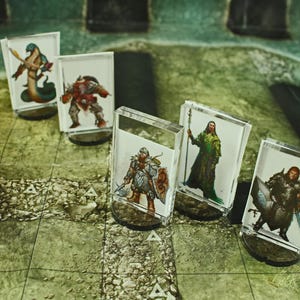 May include: Six miniature figures on clear plastic bases, each depicting a different fantasy character. The figures are arranged in a row on a green and brown surface. The figures are painted in various colors, including green, blue, red, and brown.