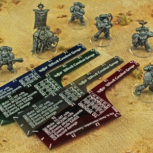 May include: Miniature figurines of space marines and combat gauges on a tan surface. The gauges are in blue, green, black, and red, with text that reads "WhvB Combat Gauge" and "To Wound". The figurines are gray.