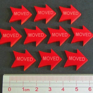 May include: Ten red arrow-shaped markers with the word "MOVED" printed in white. A ruler with centimeter markings is at the bottom. The arrows are pointing to the right.