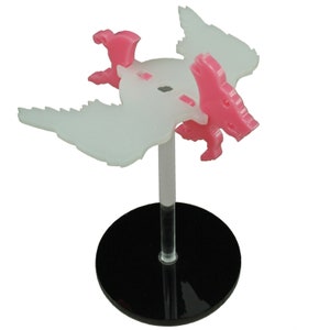 May include: A pink and white plastic miniature dragon figurine on a black base. The dragon has wings and a tail.