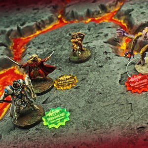May include: Miniature fantasy figures on a terrain base with a lava river. The figures include a warrior, a sorcerer, and a monster. Acrylic tokens with the words "Inspiration", "Advantage", and "Disadvantage" are also present. A tabletop game scene.