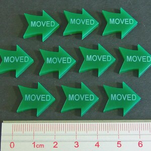 May include: Ten green arrow-shaped markers with the word "MOVED" printed in white. A ruler with centimeter markings is at the bottom of the image.