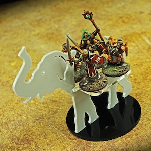 May include: A white, laser-cut elephant-shaped miniature figure base with a black circular base. Several miniature figures with swords and staffs are mounted on the elephant's back. The figures are painted with various colors.