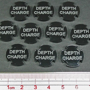 May include: Nine black plastic tokens with the words "Depth Charge" printed in white. The tokens are arranged in a circle on a gray surface with a ruler in the bottom of the image.