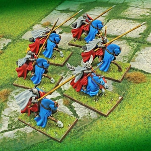 May include: Miniature figurines of knights on horseback, ready for battle. The knights wear silver armor, red and blue capes, and wield lances. The horses are blue and the bases are green, creating a medieval theme.