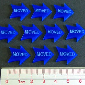 May include: Ten blue arrow-shaped tokens with the word "MOVED" printed on each. A ruler with centimeter markings is at the bottom. The tokens are arranged in three rows.