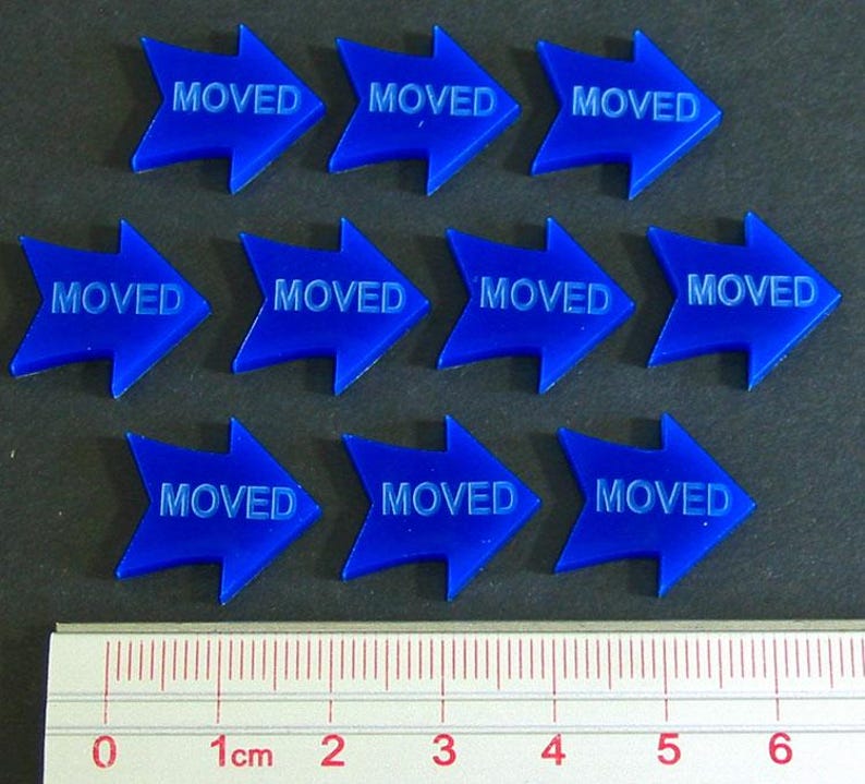 May include: Ten blue arrow-shaped tokens with the word "MOVED" printed on each. A ruler with centimeter markings is at the bottom. The tokens are arranged in three rows.