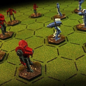 May include: Miniature figurines of robots and soldiers in red, blue, and white, arranged on a green hexagonal grid. The figures are detailed and appear to be part of a tabletop game or hobby.
