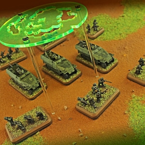 May include: Miniature military models of vehicles and soldiers on a brown surface. The models are painted in shades of green and brown, with a large green translucent structure overhead. The scene is set on a miniature battlefield.