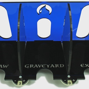May include: A blue acrylic card game organizer with three compartments labeled "Draw", "Graveyard", and "Exile". Each compartment has a counter with a number on it.