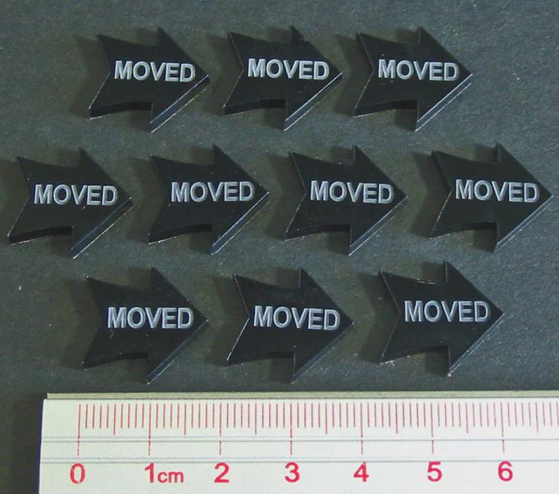 May include: Ten black arrow-shaped stickers with the word "MOVED" in white. A ruler is at the bottom, showing measurements in centimeters. The stickers are arranged in three rows.