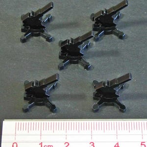 May include: Five black plastic miniature cannons on a gray surface with a ruler for scale. The cannons are about 1 cm tall.
