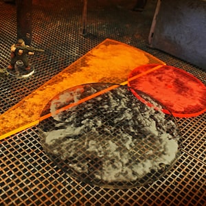 May include: A tabletop gaming scene featuring miniature figures and acrylic templates. The scene includes orange and red acrylic shapes, a textured terrain piece, and several miniature figures with weapons.