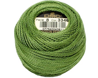 May include: A ball of green DMC Perle cotton thread, Col. 3346, with a label showing the brand and barcode. The thread is tightly wound, displaying a textured surface. The label reads "Coton Perle".