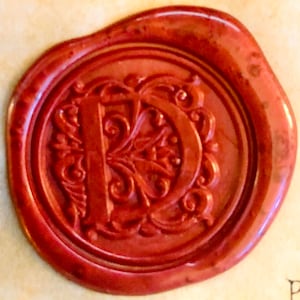 K&ouml;nnte beinhalten: Ein rotes Siegelwachs mit einem dekorativen Buchstaben "D" in der Mitte.