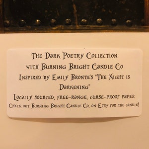 Op de afbeelding: Een witte kaart met zwarte tekst die "The Dark Poetry Collection with Burning Bright Candle Co. Inspired by Emily Bronte's "The Night is Darkening." Locally sourced, free-range, curse-proof paper. Check out Burning Bright Candle Co. on Etsy for the candle!" aankondigt.