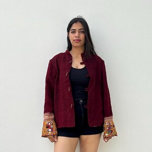 May include: A maroon jacket with embroidered details on the cuffs. The jacket has a mandarin collar and a button closure.