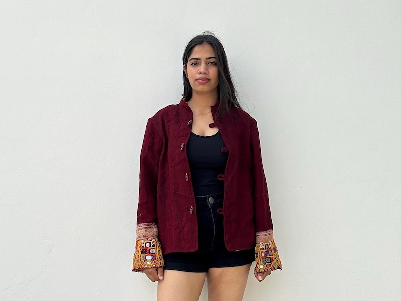 May include: A maroon jacket with embroidered details on the cuffs. The jacket has a mandarin collar and a button closure.