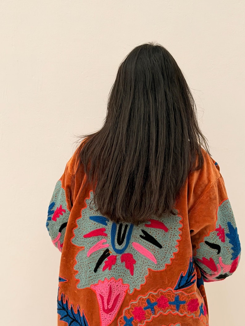 Puede incluir: Chaqueta de terciopelo naranja con intrincados bordados florales en tonos azules, rosas y verdes. La chaqueta presenta un gran dise&ntilde;o bordado en la espalda y mangas, de estilo bohemio.