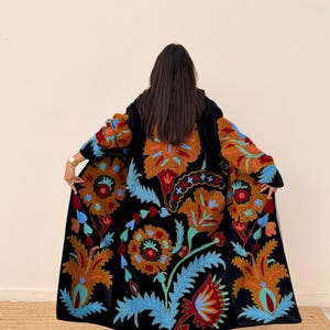May include: A black velvet coat with vibrant floral embroidery in shades of orange, red, and blue. The long coat features a detailed pattern across the front and sleeves, creating a striking visual appeal. The coat is a statement piece.