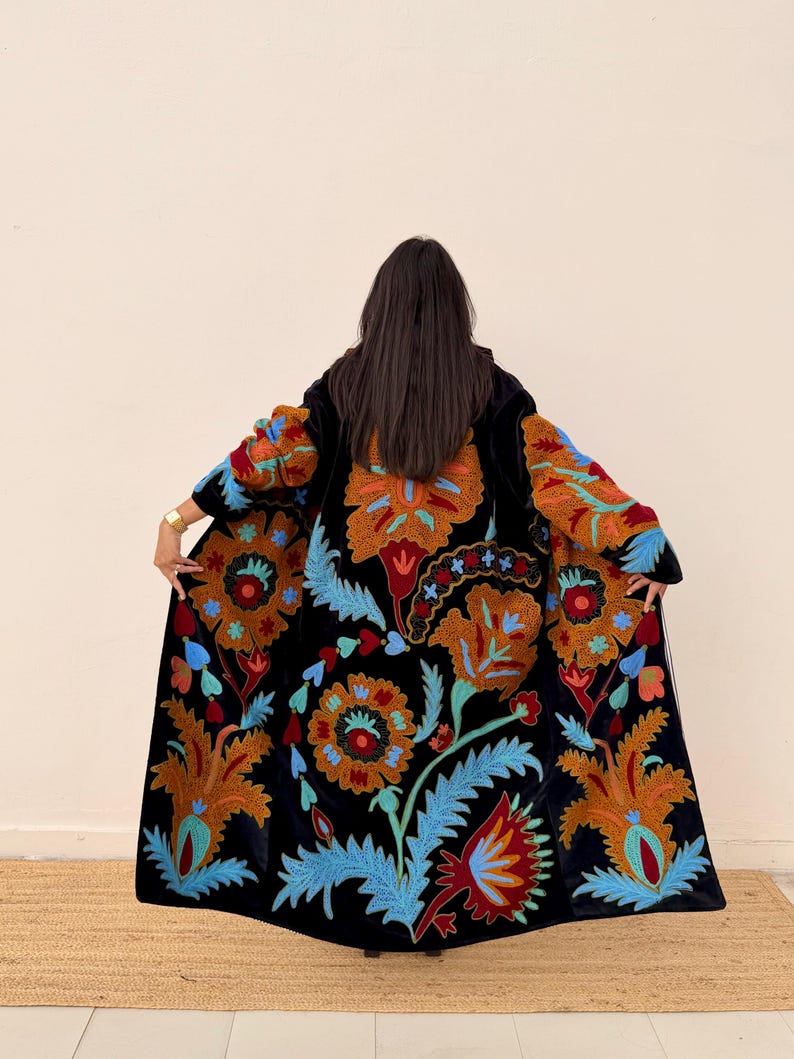 May include: A black velvet coat with vibrant floral embroidery in shades of orange, red, and blue. The long coat features a detailed pattern across the front and sleeves, creating a striking visual appeal. The coat is a statement piece.