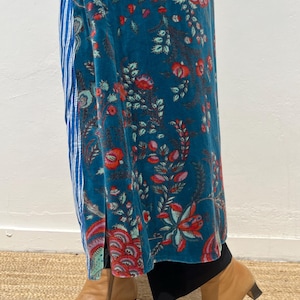May include: A teal velvet maxi skirt with a floral pattern in red and pink, paired with a blue and white striped panel. The outfit is completed with tan leather ankle boots with a small heel.