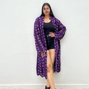 May include: A long purple and pink crocheted cardigan with a black tank top and black denim shorts.
