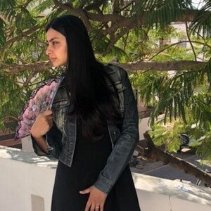 Puede incluir: Un vestido negro y una chaqueta vaquera. El vestido es de dise&ntilde;o sencillo y sin mangas. La chaqueta es de estilo vaquero cl&aacute;sico, con un lavado descolorido. La persona sostiene un abanico decorativo con motivos florales rosas y blancos.