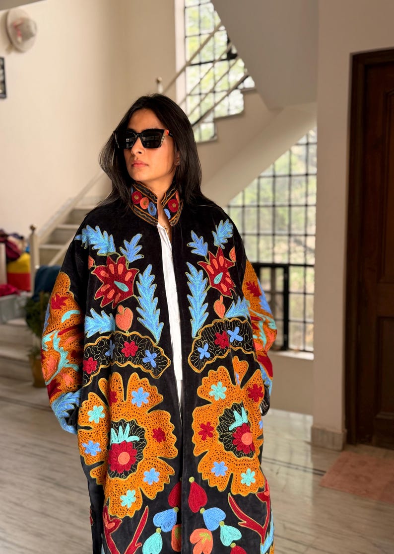 May include: Black embroidered coat with a vibrant floral design in shades of orange, red, blue, and green. The coat features a high collar and long sleeves. The embroidery is detailed and covers the front and sleeves.