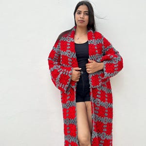 May include: A long red and gray crochet cardigan with a geometric pattern. The cardigan is open in the front and has long sleeves.