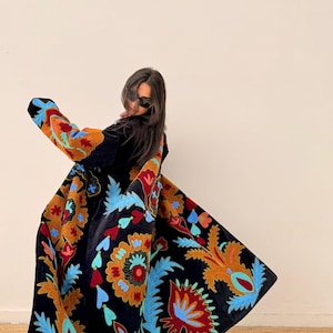 May include: A black velvet coat with colourful floral embroidery in shades of orange, blue, and red. The coat has long sleeves and a flowing design, showcasing a bohemian style. The embroidery is detailed and covers the coat's surface.