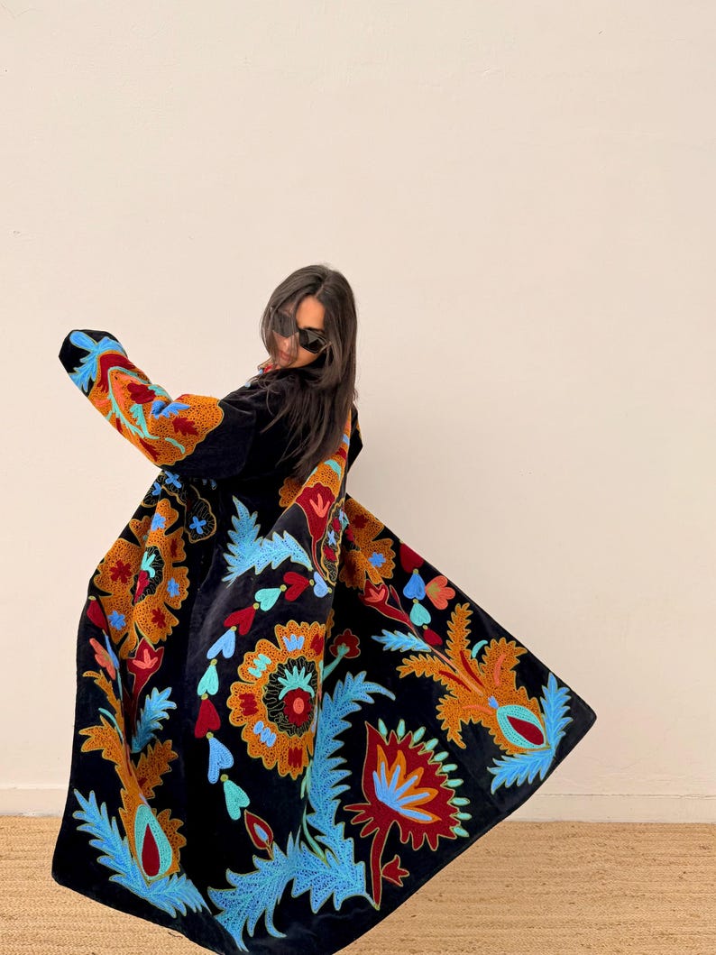 May include: A black velvet coat with colourful floral embroidery in shades of orange, blue, and red. The coat has long sleeves and a flowing design, showcasing a bohemian style. The embroidery is detailed and covers the coat's surface.